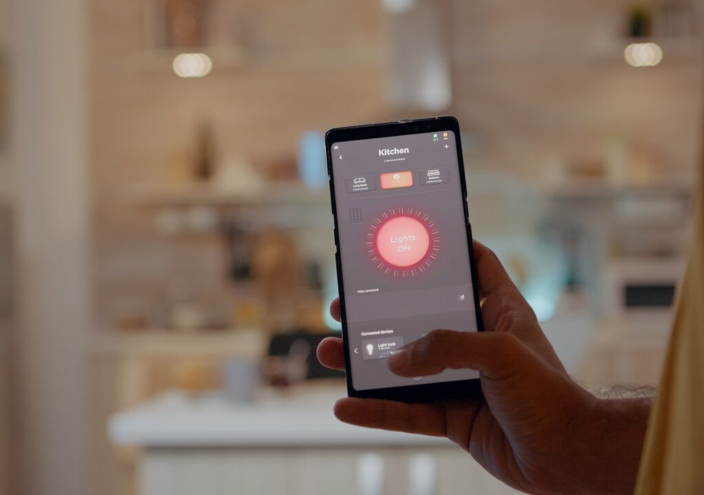 Young man using smart home application software touching screen to turn on the light by mobile phone. Male using lighting control app in house with automation system controlling efficiency of energy